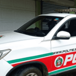 A white pickup truck with green and red stripes, labeled "Politie" and featuring a logo, is parked in front of a garage. It has a light bar on the roof, highlighting its role in the succesvolle roadblock operation, with a website URL on the side.