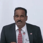 Man in pak met microfoon tijdens presentatie.