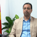 Man in pak zit naast Surinaamse vlag
